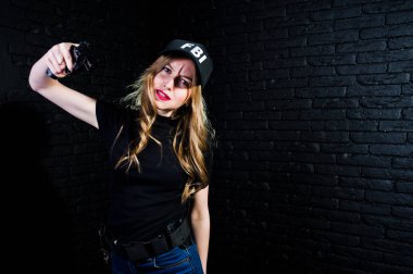 FBI kadın ajanı şapkalı ve karanlık duvara karşı stüdyoda silahla.