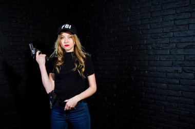FBI kadın ajanı şapkalı ve karanlık duvara karşı stüdyoda silahla.
