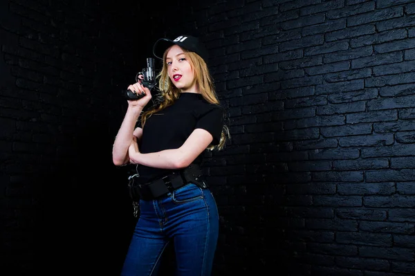 FBI kadın ajanı şapkalı ve karanlık duvara karşı stüdyoda silahla.