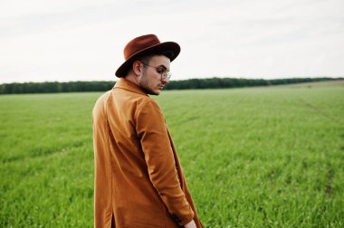 Şık adam gözlük, kahverengi ceket ve şapka yeşil sahada poz verdi..