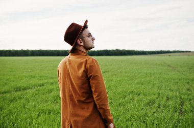 Şık adam gözlük, kahverengi ceket ve şapka yeşil sahada poz verdi..