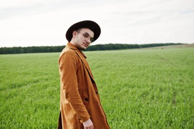 Şık adam gözlük, kahverengi ceket ve şapka yeşil sahada poz verdi..