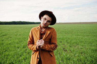 Şık adam gözlük, kahverengi ceket ve şapka yeşil sahada poz verdi..