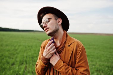 Şık adam gözlük, kahverengi ceket ve şapka yeşil sahada poz verdi..