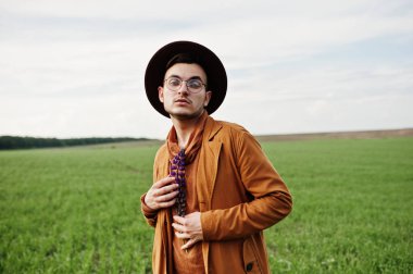 Şık adam gözlük, kahverengi ceket ve şapka yeşil sahada poz verdi..