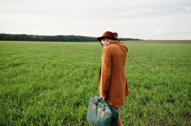 Gözlük, kahverengi ceket ve şapka çanta ile şık adam yeşil sahada poz verdi..