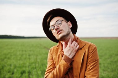 Şık adam gözlük, kahverengi ceket ve şapka yeşil sahada poz verdi..