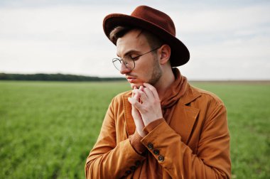 Şık adam gözlük, kahverengi ceket ve şapka yeşil sahada poz verdi..