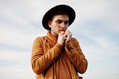 Şık adam gözlük, kahverengi ceket ve şapka yeşil sahada poz verdi..