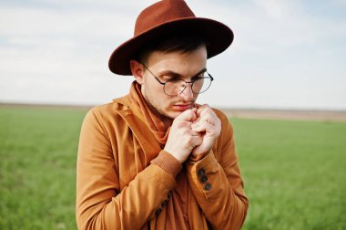 Şık adam gözlük, kahverengi ceket ve şapka yeşil sahada poz verdi..