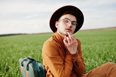 Gözlük, kahverengi ceket ve şapka çanta ile şık adam yeşil sahada poz verdi..
