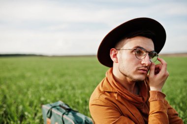 Gözlük, kahverengi ceket ve şapka çanta ile şık adam yeşil sahada poz verdi..