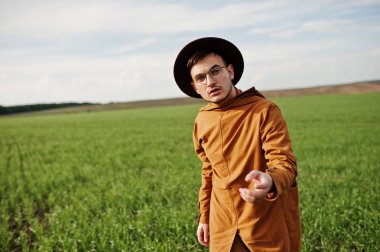 Şık adam gözlük, kahverengi ceket ve şapka yeşil sahada poz verdi..