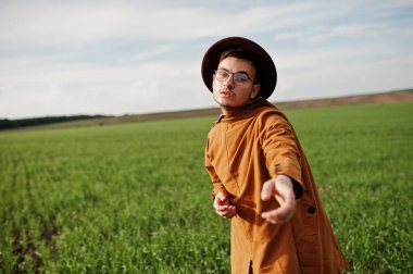 Şık adam gözlük, kahverengi ceket ve şapka yeşil sahada poz verdi..