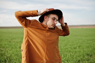 Şık adam gözlük, kahverengi ceket ve şapka yeşil sahada poz verdi..