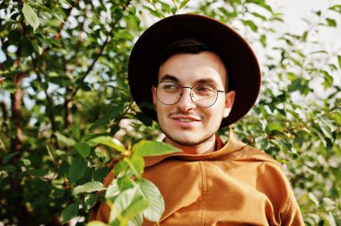 Şık adam gözlük, kahverengi ceket ve şapka yeşil sahada poz verdi..