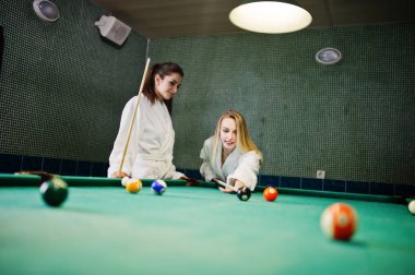 Beyaz bornoz iki seksi kızlar havuz bilardo oynamak.