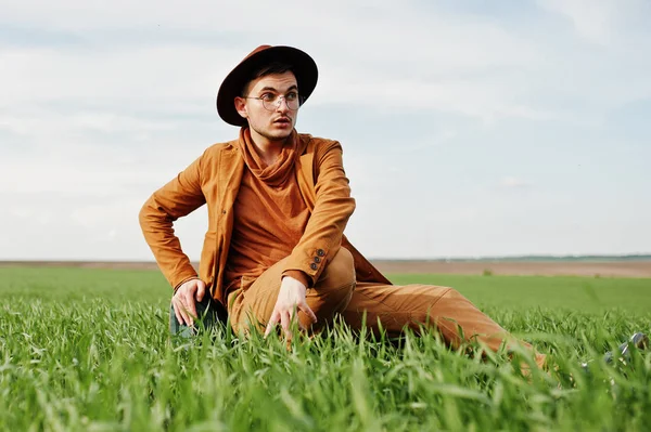 Gözlük, kahverengi ceket ve şapka çanta ile şık adam yeşil sahada poz verdi..