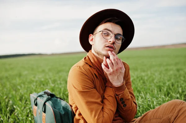 Gözlük, kahverengi ceket ve şapka çanta ile şık adam yeşil sahada poz verdi..