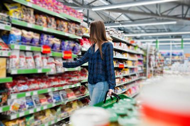 Süpermarket raflarında bakarak kadın alışveriş. Yeşil alışveriş sepeti tutan bir market mağaza genç bir kızın portresi.