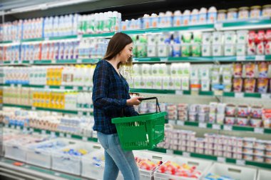 Süpermarket raflarında bakarak kadın alışveriş. Yeşil alışveriş sepeti ve süt üretim tutan bir market mağaza genç bir kızın portresi.