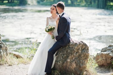 Büyük taş nehrin yanında oturan düğün çifti.