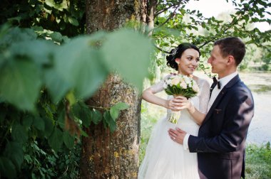 Yeni evli çift düğün gününde Gölü veya havuzda ağacın yanında poz.