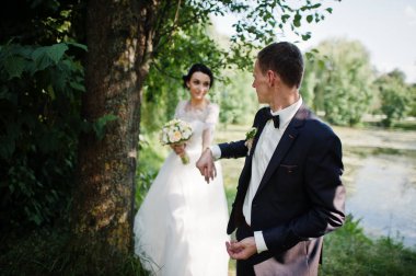 Yeni evli çift düğün gününde Gölü veya havuzda ağacın yanında poz.