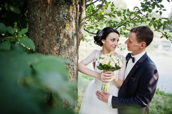 新婚のカップルは結婚式の日に湖や池のそばの木の横にポーズ — ストック写真