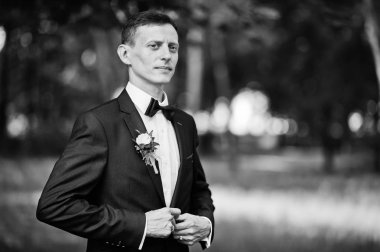 Parkta düğün gününde yalnız poz bir yakışıklı damat portresi. Siyah ve beyaz fotoğraf.