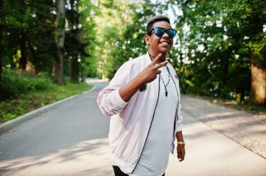 Şık hipster Arap adam adam güneş gözlüğü günbatımında sokakta açık poz verdi, iki parmak gösterir.