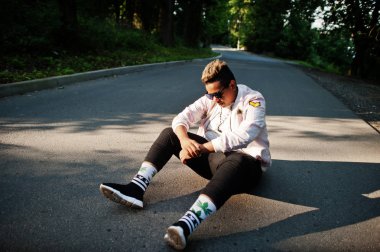 Şık hipster Arap adam adam güneş gözlüğü açık sokakta gölgeler yolu üzerinde oturan batımında poz verdi.