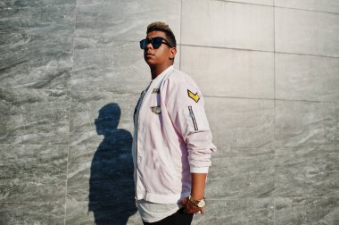 Şık hipster Arap adam adam güneş gözlüğü Caddesi'nde açık gri duvara gün batımında poz verdi.