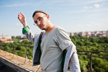 Gri takım elbise, şapka ve gözlük hayalperest şık maço adam çatıda poz verdi.. 