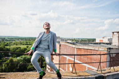 Gri takım elbise, şapka ve gözlük hayalperest şık maço adam çatıda poz verdi.. 