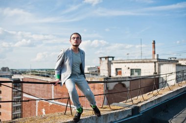 Gri takım elbise, şapka ve gözlük hayalperest şık maço adam çatıda poz verdi.. 