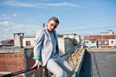 Gri takım elbise, şapka ve gözlük hayalperest şık maço adam çatıda poz verdi.. 