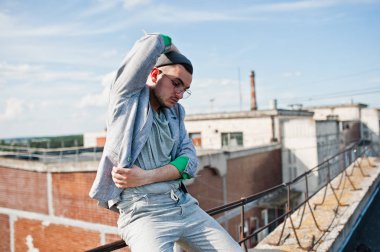 Gri takım elbise, şapka ve gözlük hayalperest şık maço adam çatıda poz verdi.. 