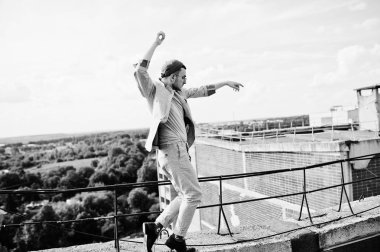 Gri takım elbise, şapka ve gözlük hayalperest şık maço adam çatıda poz verdi.. 