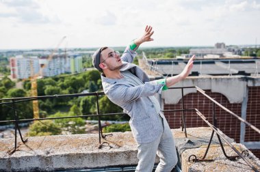 Gri takım elbise, şapka ve gözlük hayalperest şık maço adam çatıda poz verdi.. 