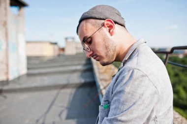 Gri takım elbise, şapka ve gözlük hayalperest şık maço adam çatıda poz verdi.. 