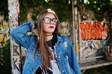 Şık casual hipster kız kot giyim ve gözlük karşı büyük grafiti duvar.