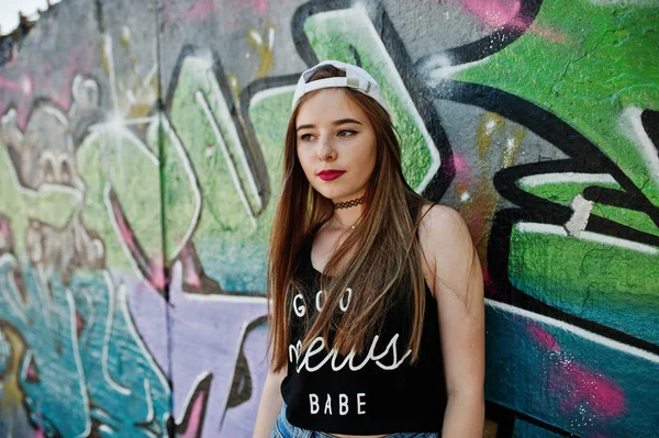 大きな落書きの壁に対してキャップ ジーンズ着用でスタイリッシュなカジュアルな内気な少女 — ストック写真
