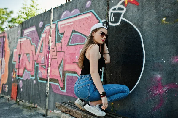 臀部时尚休闲时髦女孩在帽子 太阳镜和牛仔裤穿 听音乐从手机耳机对大涂鸦墙大 Tnt — 图库照片