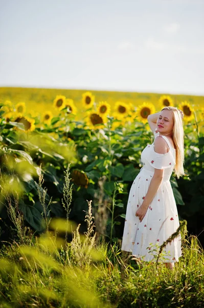 Blonde pregnant mother in sunflowers field. Happy moments of pregnancy.