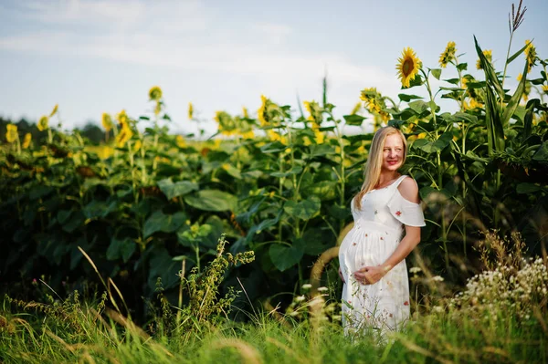 Blonde pregnant mother in sunflowers field. Happy moments of pregnancy.