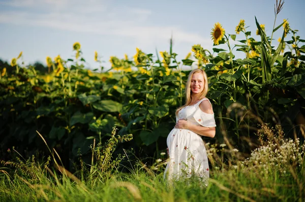 Blonde pregnant mother in sunflowers field. Happy moments of pregnancy.
