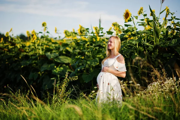 Blonde pregnant mother in sunflowers field. Happy moments of pregnancy.