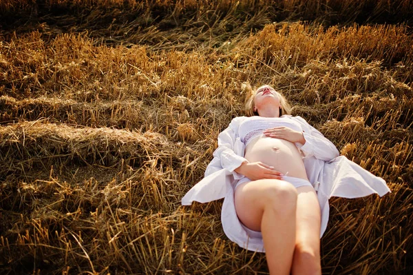 Blonde pregnant woman in wreath field at white underwear clothes on sunset. Happy moments of pregnancy.