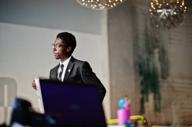 Afrika kökenli Amerikalı işadamı giymek siyah takım elbise ve gözlük ofis, iş günü önce sabah kahve içme.